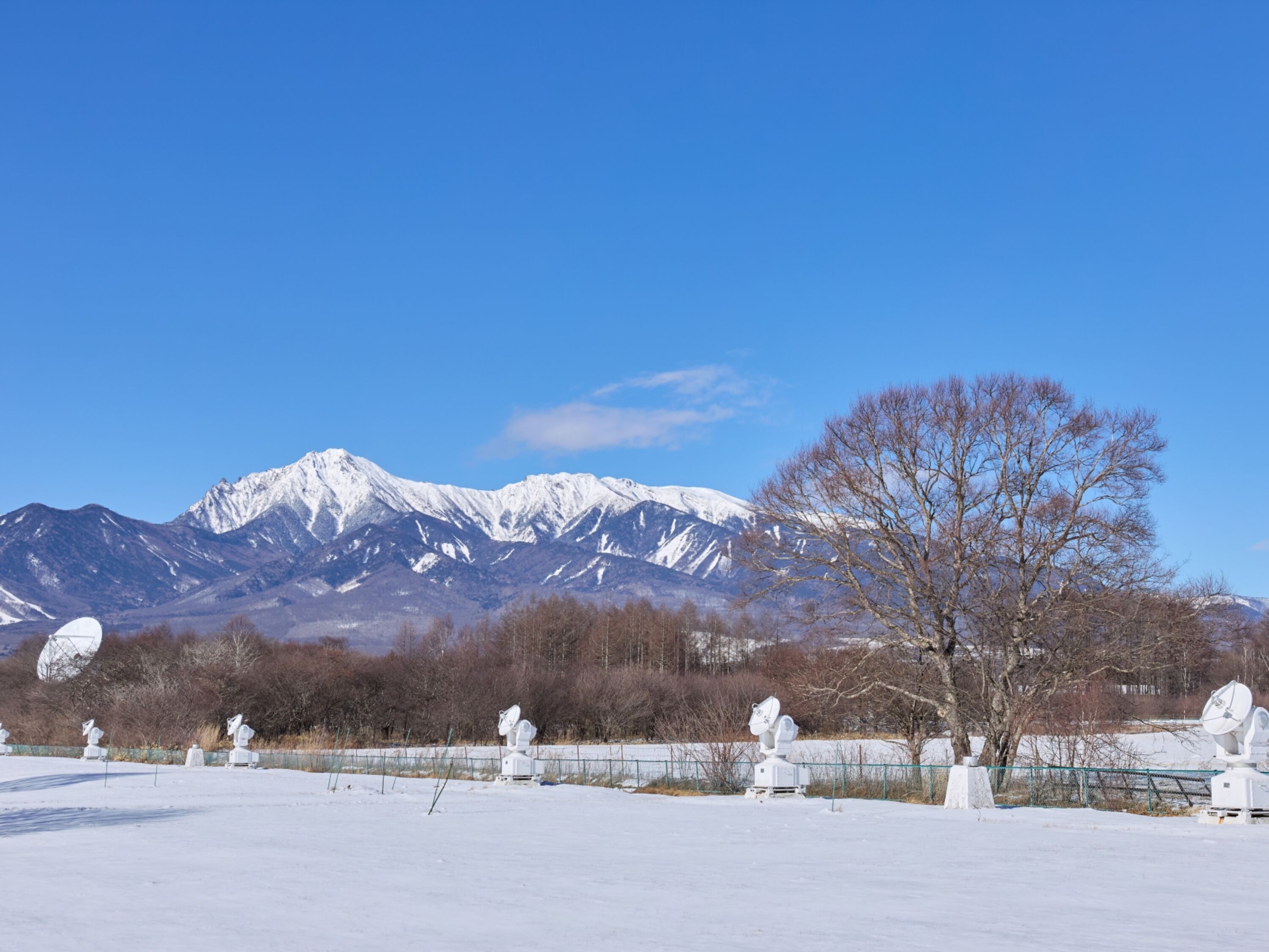 A snowy landscape with mountains in the background and a fenced area with satellite dishes.