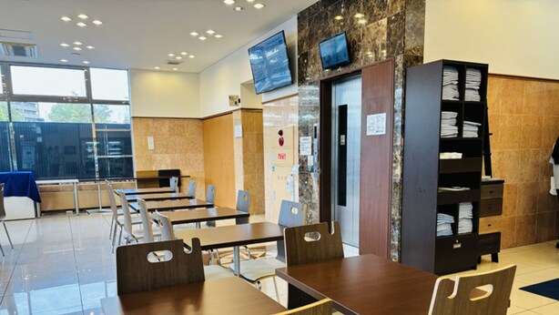 A modern dining area with wooden tables and chairs, a television mounted on the wall, and a counter with a menu board. - Toyoko Inn Sakudaira Station Asama (Saku)