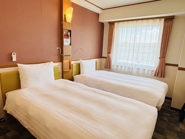 Habitación de hotel con dos camas, una mesita de noche, una lámpara, una ventana con cortinas y un teléfono en la pared.