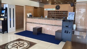 A reception area with a 'FRONT' sign, a clock, a counter with a computer, a small seating area, and a vending machine. - Toyoko Inn Sakudaira Station Asama (Saku)