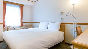 A hotel room with a large bed, a desk, a chair, a lamp, and a window with curtains.