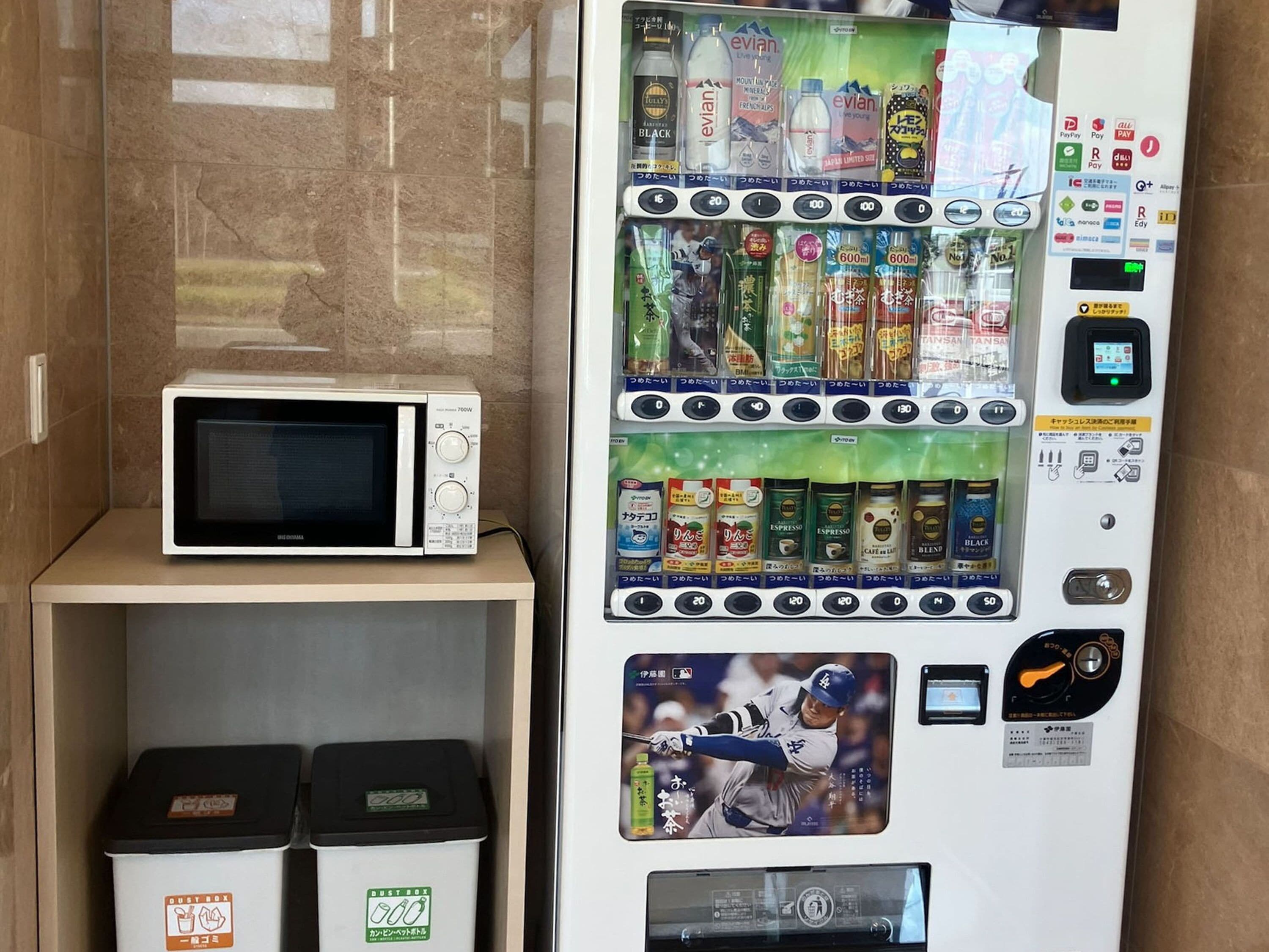 Máquina expendedora con diversas bebidas y aperitivos, un microondas y botes de basura.