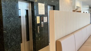 A reception area with marble walls, a beige bench, and two elevators. - Toyoko Inn Chiba-minato Ekimae (Chiba)