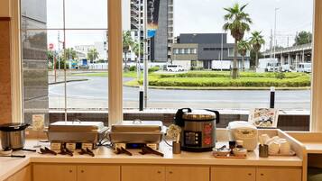 A kitchen counter with cooking appliances and utensils, a window with a view of a city street and palm trees.