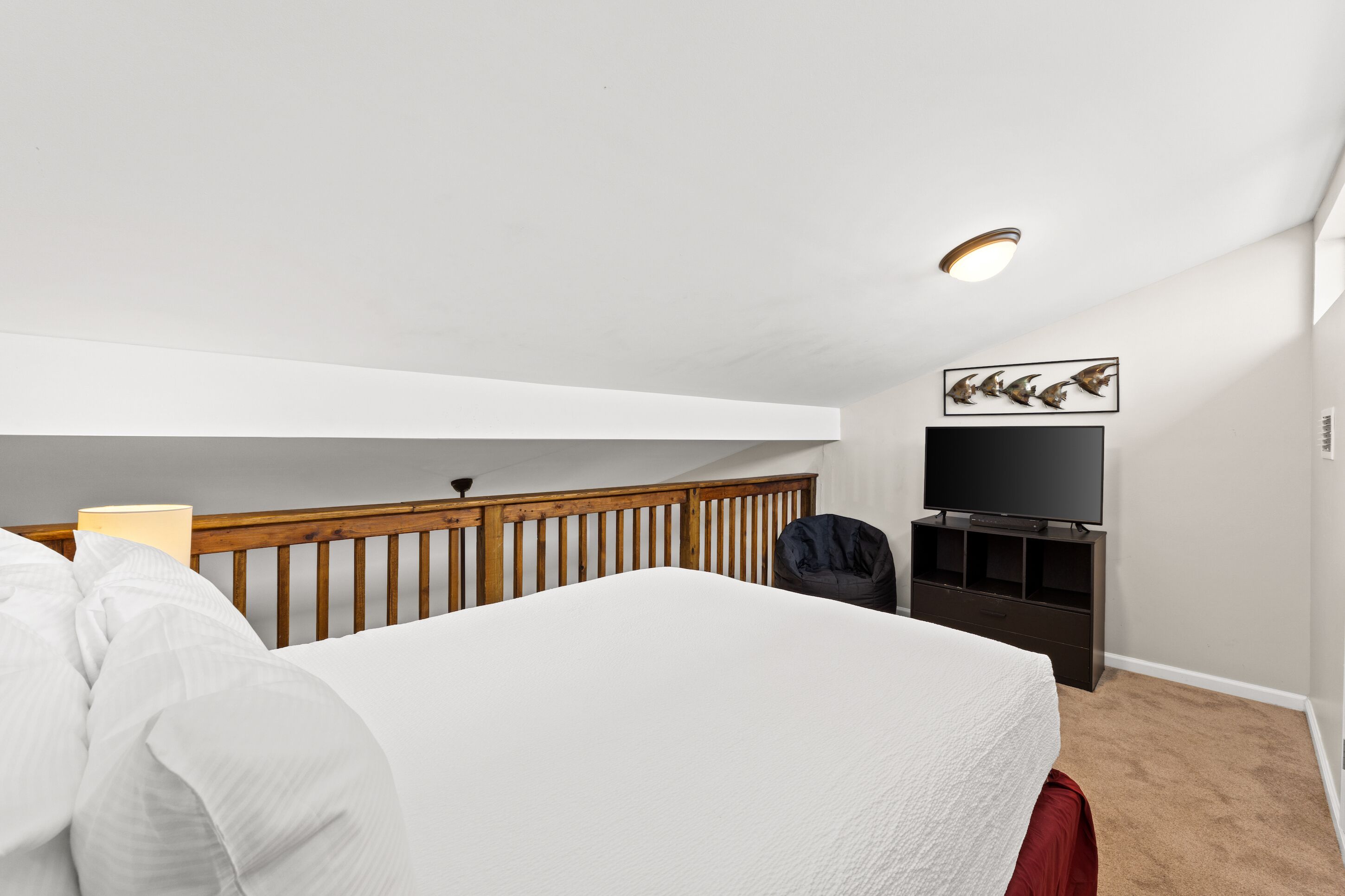 A bedroom with a bed, a TV, a wooden railing, and a ceiling light.