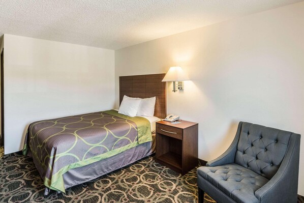 A hotel room with a bed, a nightstand with a lamp, and a chair. - Rodeway INN (Leadville)