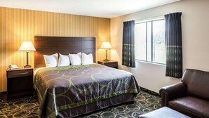 Een hotelkamer met een groot bed, twee nachtkastjes met lampen, een leren fauteuil en een raam met gordijnen.