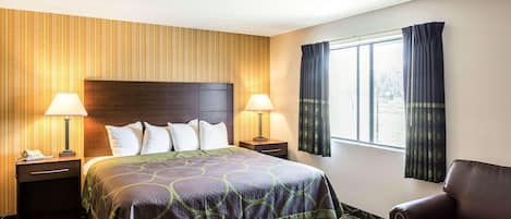 A hotel room with a large bed, two bedside tables with lamps, a leather armchair, and a window with curtains.