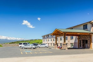 A hotel with a covered parking area, a stone facade, and a view of mountains in the background. - Rodeway INN (Leadville)