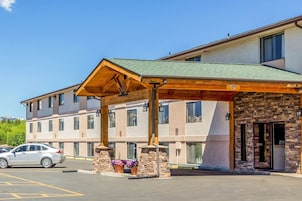 Un hotel con entrada cubierta, estacionamiento exterior y fachada de piedra.
