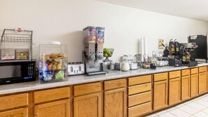 Een kitchenette met een magnetron, broodrooster, koffiezetapparaat en diverse etenswaren.