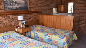 Una habitación con dos camas, cabecera de madera, una mesita con lámpara y un cuadro en la pared.