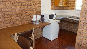 Una cocina con pared de ladrillo, un refrigerador blanco, un microondas, un lavamanos y una mesa de madera con sillas.