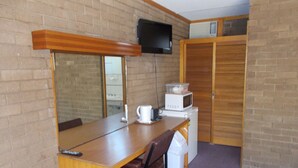 Habitación pequeña con una mesa de madera, una silla marrón, un microondas y un televisor fijado a la pared.