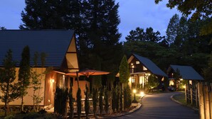 A modern lodge with a curved driveway, outdoor seating, and a well-lit entrance. - Pica Yamanakako Village (Yamanakako)