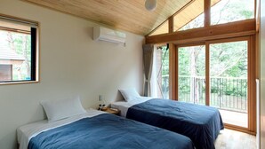 A room with two beds, a ceiling fan, an air conditioning unit, and large windows with a view of trees. - Pica Yamanakako Village (Yamanakako)
