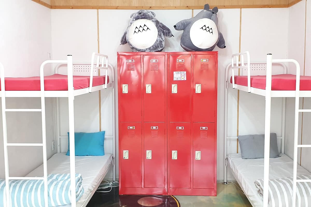 A bunk bed room with two bunk beds, a red set of lockers, and two stuffed animals on top.