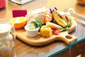 A wooden cutting board with a variety of food items including corn, tomatoes, lettuce, and fried items. - Ocean Lover Homestay (Hualien City)