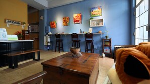 A room with a wooden table, chairs, a bench, and a sofa. There are paintings on the wall and a shelf with books and a plant. - Ocean Lover Homestay (Hualien City)