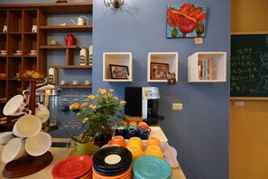 A kitchen area with various dishes, a coffee machine, and a wall with shelves containing kitchenware and framed photos.
