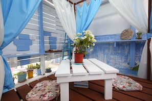 A white wooden bench with a potted plant, surrounded by blue and white curtains, and small cushions.