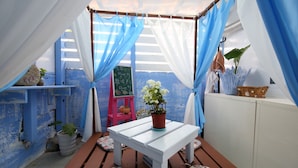 A small, enclosed patio area with a white table and floral cushions, blue and white curtains, and potted plants. - Ocean Lover Homestay (Hualien City)