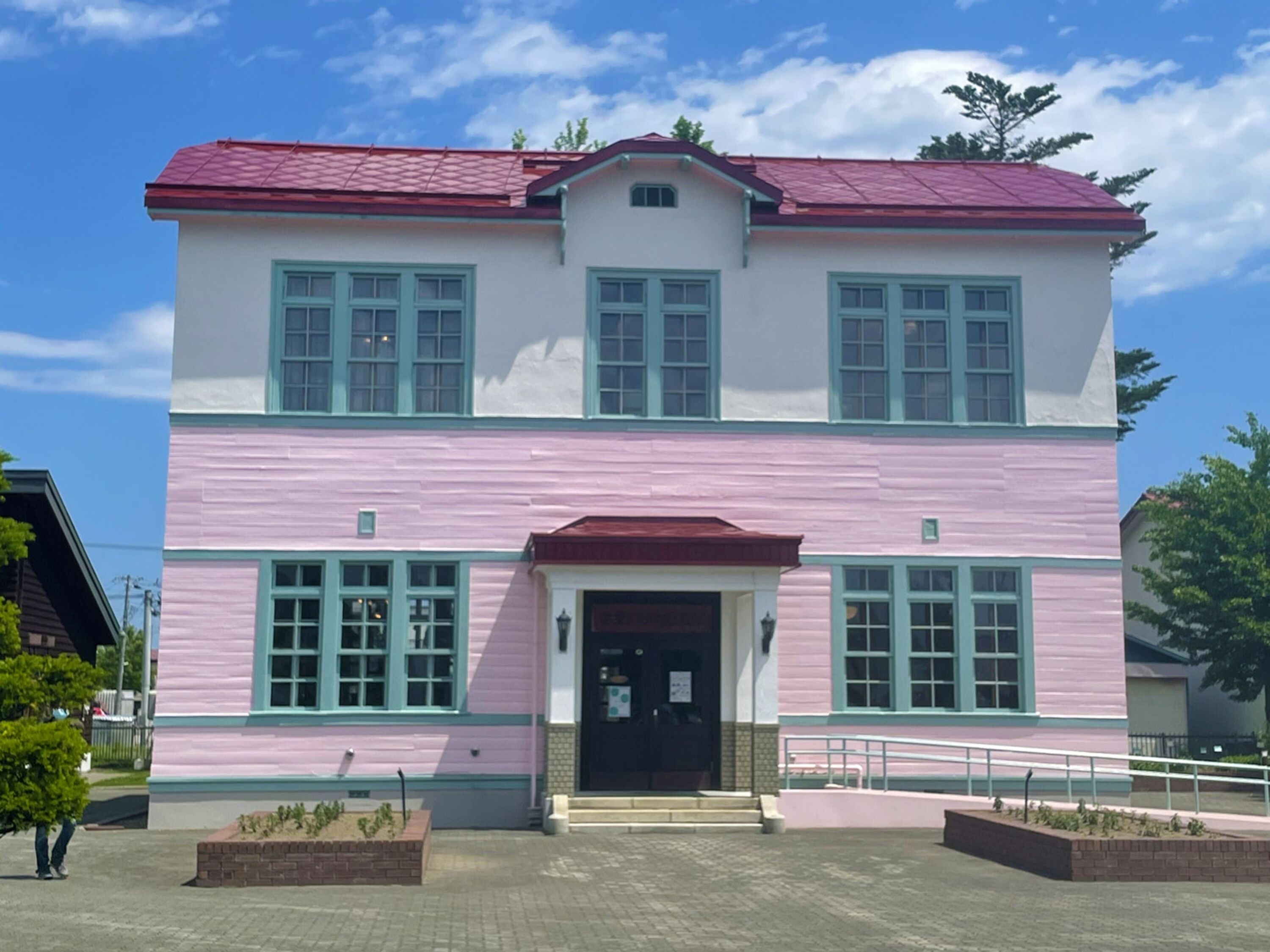 A two-story building with a red roof and pink walls, featuring a central entrance with steps and a small porch.