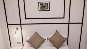 A neatly made bed with two pillows, a framed picture on the wall, a bedside table with a lamp, and a towel on the bed. - The Loft Room Ubon (Ubon Ratchathani)