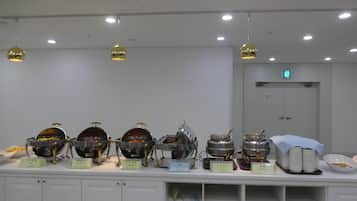 A buffet setup with various food containers and serving utensils, a white cabinet with labels, and a door with an emergency exit sign.