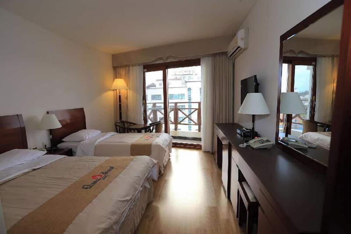 Ein Hotelzimmer mit zwei Betten, einem Schreibtisch, einem Sessel, einem Fernseher und einem Balkon mit Blick.