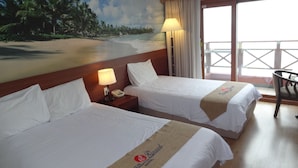 Habitación de hotel con dos camas, un mural de una playa, un balcón con una silla y una lámpara.