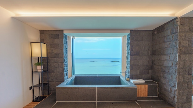 Un baño moderno con bañera integrada, paredes de piedra y vista al mar.