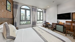 Habitación de hotel con cama, dos ventanas, escritorio con televisor y un refrigerador pequeño.