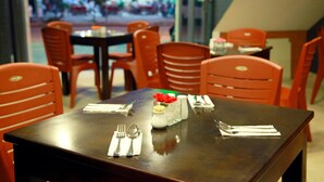 Un restaurante con una mesa de madera oscura dispuesta para dos personas, sillas anaranjadas y vistas a una calle concurrida.