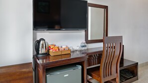 Habitación de hotel con escritorio de madera, televisor, espejo, refrigerador pequeño y una silla.