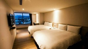 Habitación de hotel con dos camas, un televisor, un escritorio y un ventanal con vistas a la ciudad.