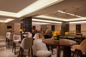 Un vestíbulo de hotel moderno con mesas redondas, asientos cómodos y arreglos florales decorativos.