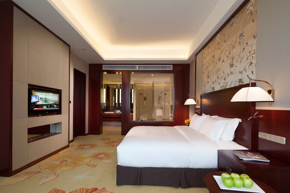 Habitación de hotel con una cama grande, televisión, mesita de noche con lámpara y baño a la vista a través de una puerta abierta.