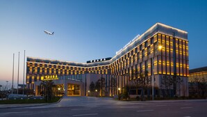 Un hotel moderno junto al aeropuerto, con una entrada destacada, varios pisos y un frente bien iluminado.