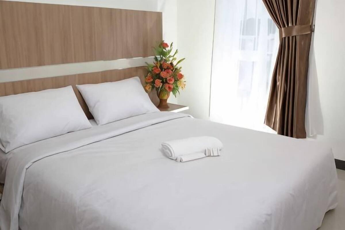 A neatly made bed with white linens, a wooden headboard, and a vase of flowers on a bedside table.