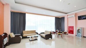 A modern hotel lobby with a sofa set, a coffee table, a dining area with chairs, and a red vending machine. - Hotel Sakura Manado (Manado)