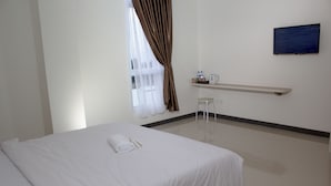 A hotel room with a bed, a small table with a chair, a shelf with toiletries, and a TV on the wall. - Hotel Sakura Manado (Manado)