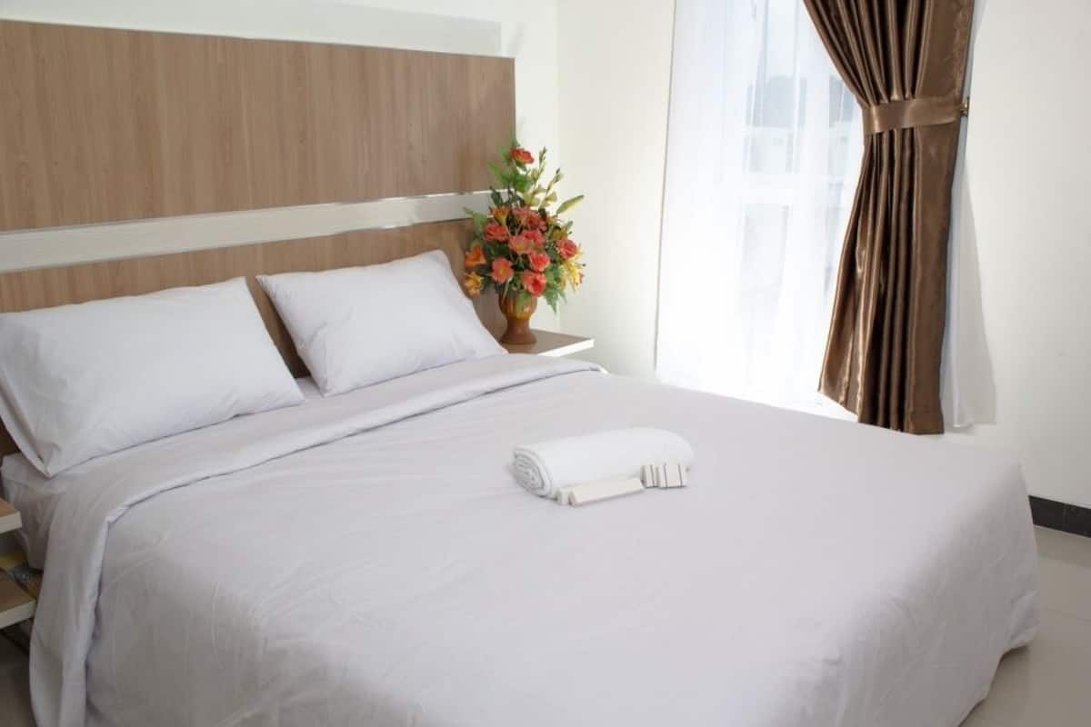 A neatly made bed with white linens, a wooden headboard, and a vase of flowers on a bedside table.