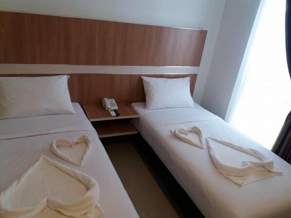 A hotel room with two beds, a wooden headboard, a bedside table with a phone, and heart-shaped towels on the beds. - Hotel Sakura Manado (Manado)