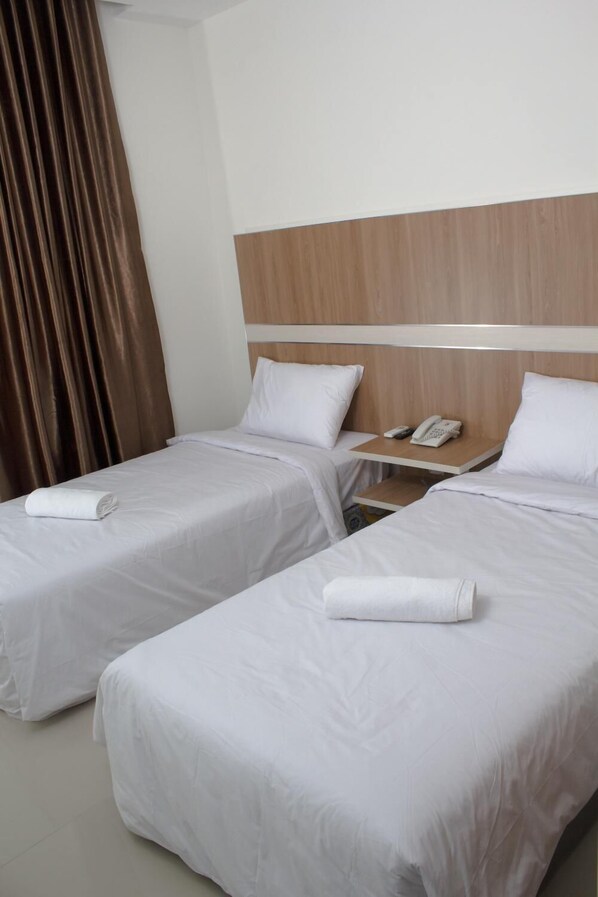 Une chambre d’hôtel avec deux lits simples, une tête de lit en bois, une table de chevet avec un téléphone et un rideau.