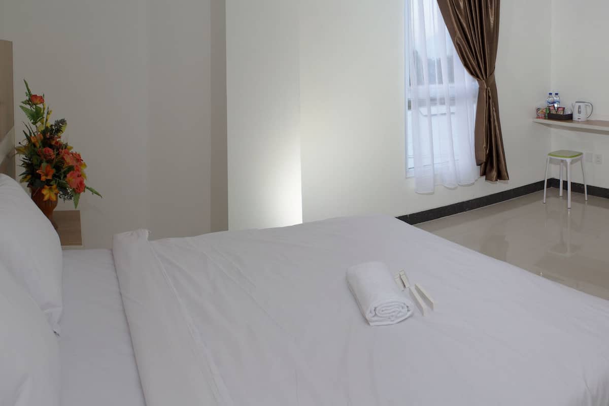 A hotel room with a neatly made bed, a small table with a kettle and water bottles, a chair, and a TV on the wall.
