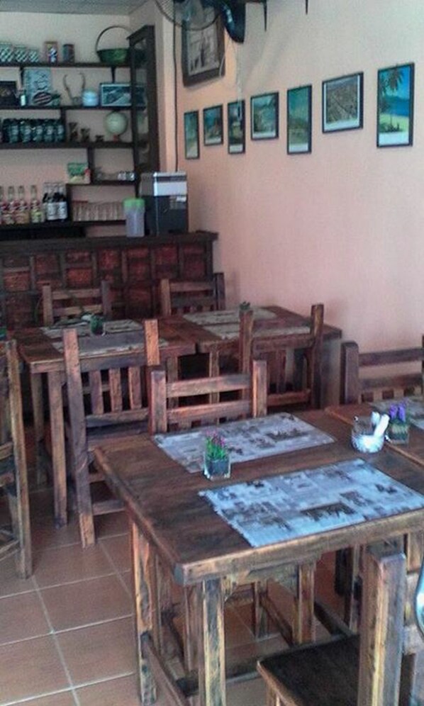 Un comedor rústico con mesas y bancos de madera, una zona de bar con estantes llenos de botellas, y una pared decorada con cuadros enmarcados.