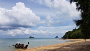 Une plage avec un bateau amarré près du rivage, une eau calme et des îles lointaines.