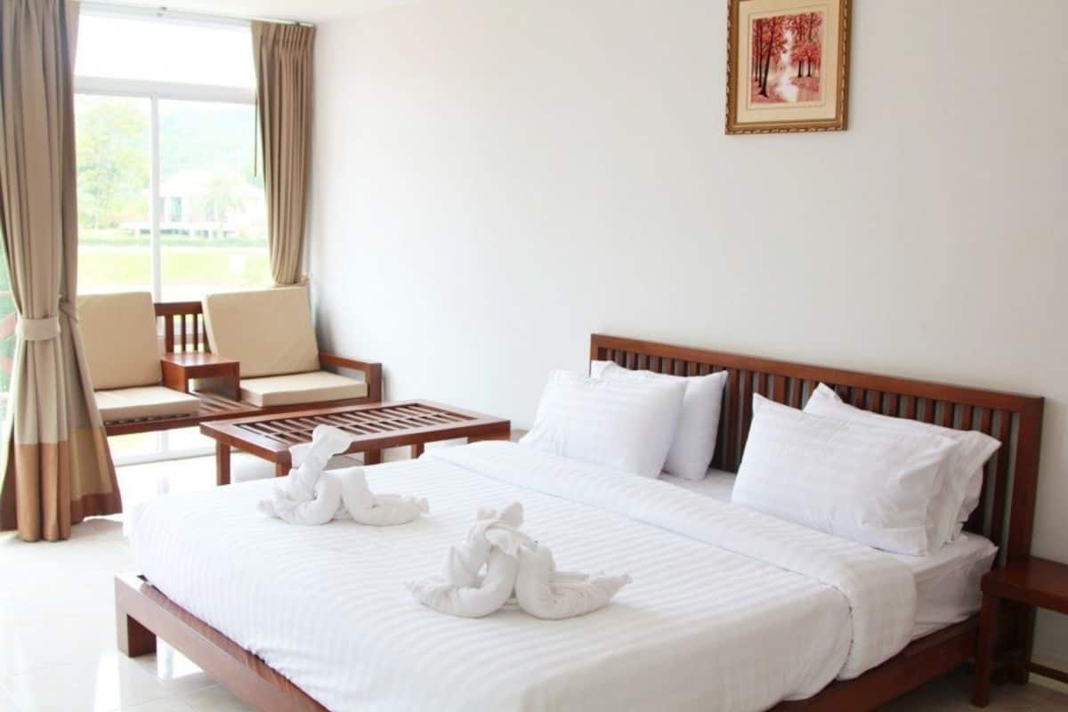 Habitación de hotel con una cama grande, dos almohadas blancas con forma de cisne, un cabecero de madera, una mesita pequeña y una silla.
