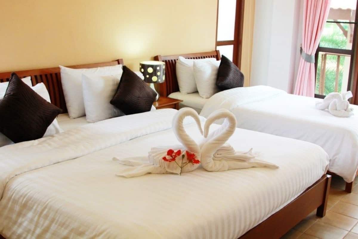 Habitación de hotel con dos camas, cada una con ropa blanca y almohadas marrones. En la cama del primer plano se ve un diseño de toalla con forma de corazón.